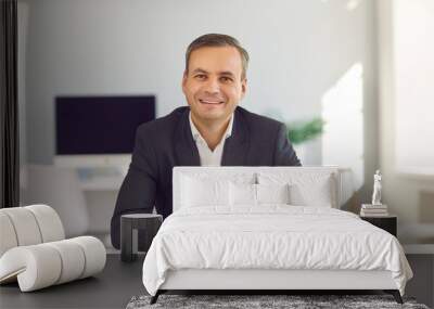 Young smiling businessman sitting and looking at camera during online videocall in office Wall mural