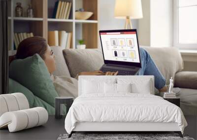 young woman lying relaxing on sofa at home shopping online on internet on computer. millennial girl  Wall mural