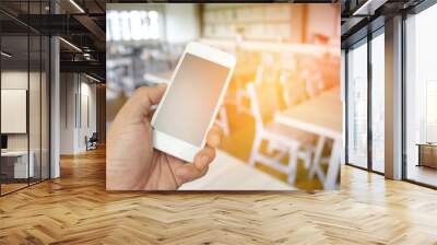 hand holding the smartphone on blur restaurant background with b Wall mural