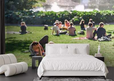 Relaxing summer day in a Danish park, people lounging on the grass, pond water in the background. Concept of hygge. Wall mural