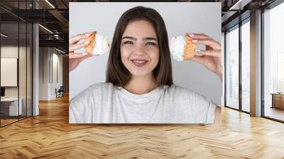 young beautiful funny woman holding two sweet cupcakes with cream near her head smiling looking happy isolated white background healthy lifestyle Wall mural