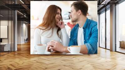 young couple beautiful woman holding hands with her handsome man looking each other in the eyes while drinking coffee in cafe , love and tenderness concept Wall mural