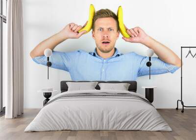 young handsome man holding two fresh bananas near his head looking funny on isolated white background Wall mural