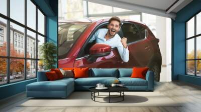 young handsome man looking for new car in dealership center sticking out the vehicle window Wall mural