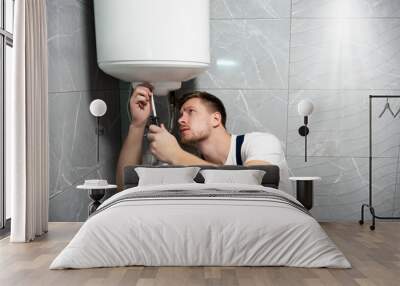 young handsome smiling man worker in uniform with screwdriver in his hand repairing boiler at home in the toilette professional repair service Wall mural