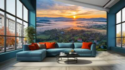 Aerial footage with layers of fog hanging over a rural town and scenic landscape at a beautiful dramatic sunrise with the glowing sun Wall mural