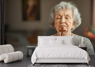 Portrait of senior woman praying while holding Christian symbol of crucifix Old woman praying to god with hope and closed eyes. Elderly believers make a prayer with faith holding rosary in their hands Wall mural