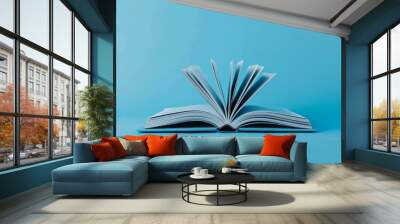 Open book with flipping pages isolated on blue background, concept of knowledge, education, literature, and learning resources for academic, professional, or creative projects Wall mural