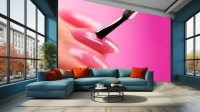 Applying Nail polish, pink shellac UV gel, varnish, nails manicure process concept in beauty salon. Transparent top coat drop on brush. Over pink background. Application of nail polish Wall mural