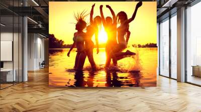 Beach party. Group of happy girls dancing in water on beautiful summer sunset. Wall mural