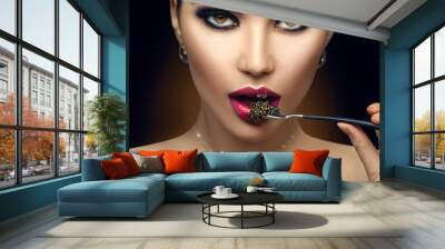 Beautiful Fashion Model woman eating black caviar. Beauty girl portrait with caviar on her lips. Fashion female with spoon of black Caviar isolated on Black background, closeup Wall mural