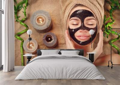 Beautiful woman with black purifying black mask on her face. Beauty model girl with black facial peel-off mask lying in spa salon. Skincare, cleansing Wall mural