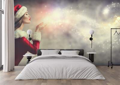 Christmas scene. Sexy Santa. Brunette young woman in party costume blowing snow over holiday blurred background Wall mural