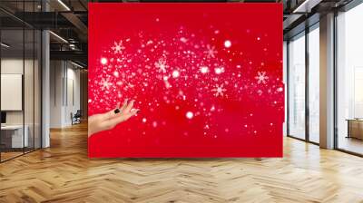 Christmas winter fashion girl on red background. Beautiful New Year and Xmas holiday makeup. Beauty model woman in Santa's hat blowing snow in her hand Wall mural