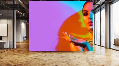 High Fashion model woman portrait in colourful bright neon lights, beautiful party girl with trendy make-up, manicure, hairstyle. Pointing hand, advertising gesture over colorful vivid background. Wall mural