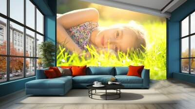 Portrait of a smiling little girl lying on green grass. Cute six years old child enjoying nature in summer park on a lawn Wall mural