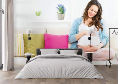 Pregnant woman sitting on a sofa and caressing her belly Wall mural