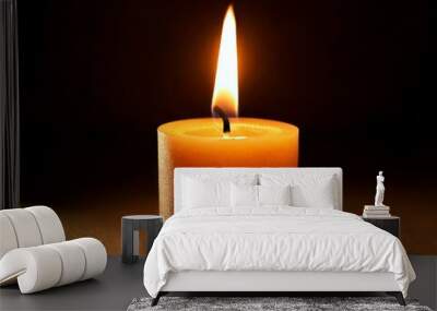 A close-up of a single lit candle glowing in the darkness, creating a warm and calming atmosphere. Wall mural