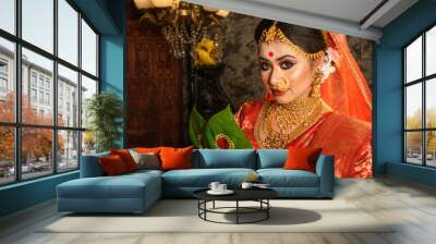 Portrait of very beautiful Indian bride holding betel leaf, Bengali bride in traditional wedding saree with makeup and heavy jewellery in studio lighting indoor Wall mural