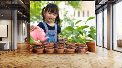 Adorable 3 years old asian little girl is watering the plant  in the pots outside the house, concept of plant growing learning activity for preschool kid and child education for the tree in nature Wall mural