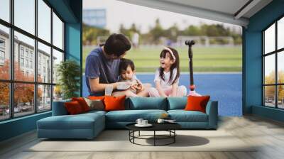 Asian father and child sitting in stadium after exercise time, they relaxing talk and laughing together with happiness moment, concept of sport and outdoor activity, quality time spending in family. Wall mural