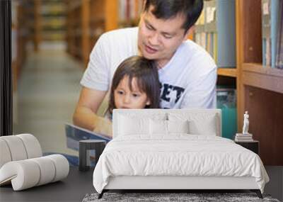 Asian father and daughter are reading story book together in the library, concept of learning activity for kid development in family lifestyle. Wall mural