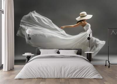 A woman in a white dress and a summer hat looks like she's flying in front of a gray background. She could be a bride in a wedding dress or just a beautiful girl in a long, flowing silk dress. Wall mural