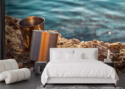 two metal cup on the rocks at the holiday with blue sea. camping, drinking and summer concept. Wall mural