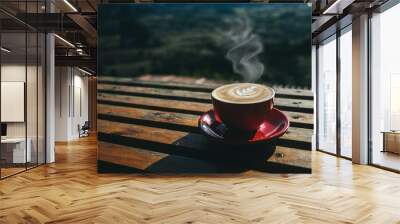 A cup of hot coffee or cappuccino is placed on an outdoor wooden table in the morning by the smoke rising from the red cup. Wall mural