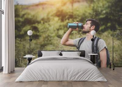 Camping concept - Man traveler drank water from a glass bottle held in his hand. Wall mural