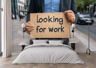 A person is holding a sign that reads 'Looking for work' in a busy urban setting, capturing the essence of job searching. Wall mural