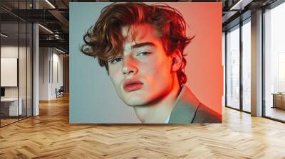 A stylish young man with tousled hair poses against a vibrant background, showcasing modern fashion and youthful confidence. Wall mural