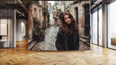 Satisfied woman in casual attire, standing against a backdrop of a charming, historic European street with cobblestone paths and old buildings Wall mural