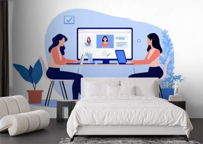 Two women engaged in a virtual meeting, interacting with laptops and a large screen displaying profiles in a modern workspace. Wall mural