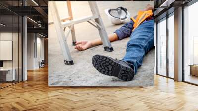 Accident and injury on a construction site. Safety first concept. Male worker lying down unconscious on the floor with safety helmet after falling from ladder. Fainting from exhaustion or heat stroke Wall mural