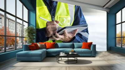 Building inspector man using digital tablet checking safety and security system in the building. Asian male worker in reflective vest working for building maintenance inspection Wall mural