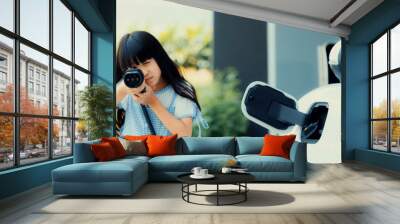 A playful girl holding and pointing an EV plug, a home charging station providing a sustainable power source for electric vehicles. Concept of progressive new generation with ecological awareness. Wall mural