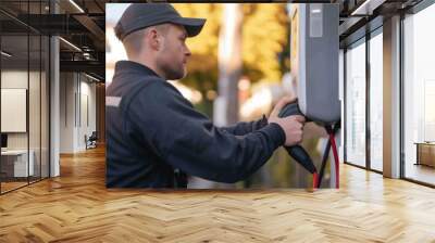 A technician in high-visibility clothing installs an electric vehicle charger, contributing to the infrastructure of sustainable transportation. AIG41 Wall mural