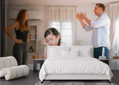 Annoyed and unhappy young girl sitting on sofa trapped in middle of tension by her parent argument in living room. Unhealthy domestic lifestyle and traumatic childhood develop to depression Synchronos Wall mural