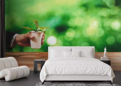 Businessman holding plant pot with his hand promoting forest regeneration and natural awareness. Ethical green business with eco-friendly policy utilizing renewable energy to preserve ecology. Alter Wall mural