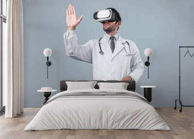 Caucasian doctor looking medical data while using VR goggles to connect metaverse. Skilled doctor standing while holding and pointing at something while wearing lab coat and visual reality. Deviation. Wall mural