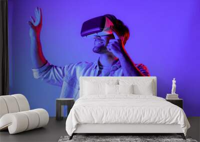 Caucasian man enter metaverse by using virtual digital goggles while standing look in cyberspace display virtual world. Sport gamer with casual cloth move gesture at neon background. Tech. Deviation. Wall mural