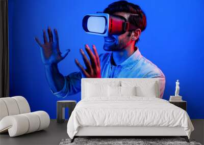 Caucasian smart man holding and moving gesture while using VR goggle. Happy person using headset and goggle while enter virtual world or metaverse with neon light background. Technology. Deviation. Wall mural