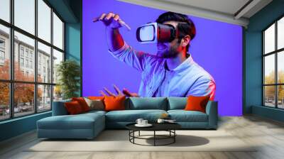 Caucasian smart man holding and moving gesture while using VR goggle. Happy person using headset and goggle while enter virtual world or metaverse with neon light background. Technology. Deviation. Wall mural