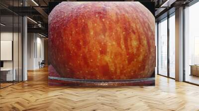 Close-up showcases a crisp bright red fresh apple nestled comfortably in a glass bowl. The black background creates a dramatic stage, highlighting the apple's flawless and smooth skin. Comestible. Wall mural