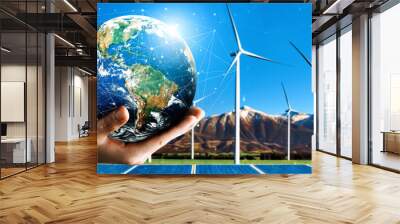 Concept of sustainability development by alternative energy. Man hand take care of planet earth with environmentally friendly wind turbine farm and green renewable energy in background. uds Wall mural