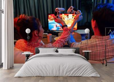 Couple gamer with hands cross of joystick playing fighting competition video game together on tv screen at back side view, sitting sofa at neon light color living room at modern comfy home. Infobahn. Wall mural