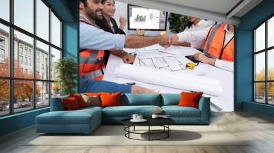 Diverse group of civil engineer and client celebrate and high five after make successful agreement on architectural project, reviewing construction plan and building blueprint at meeting table.Prudent Wall mural