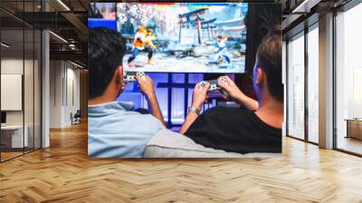 Friend gamers playing video game of battle martial arts fighter on TV using joysticks position of backside background. Comfy living neon light at home place with cheerful fighting winner. Sellable. Wall mural