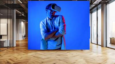 Handsome smart man dancing and moving gesture to music by using VR glasses with neon light background. Caucasian male gamer standing while moving to pop music wearing technology innovation. Deviation. Wall mural